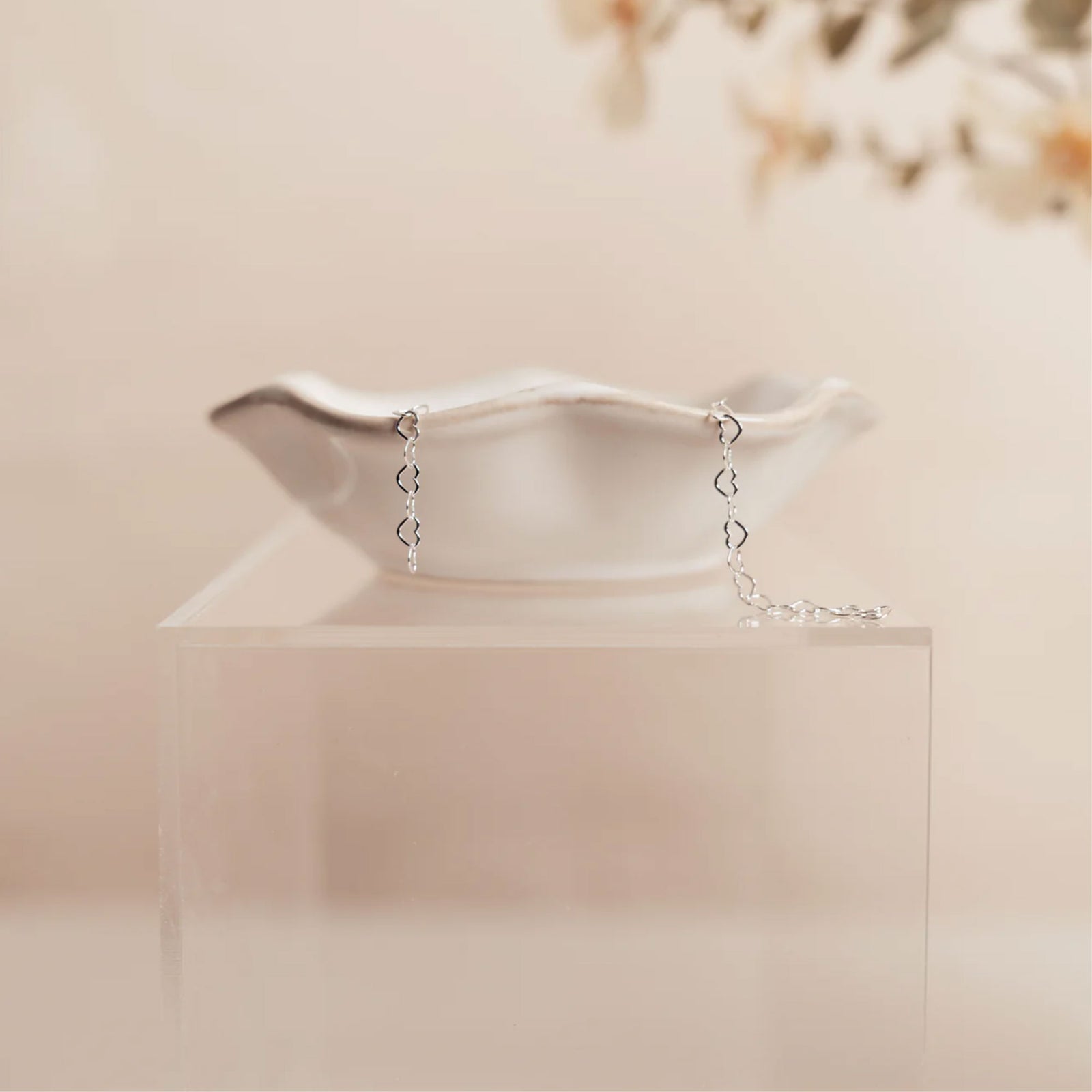 Silver bracelet with heart-shaped charms on a clear stand against a soft beige background