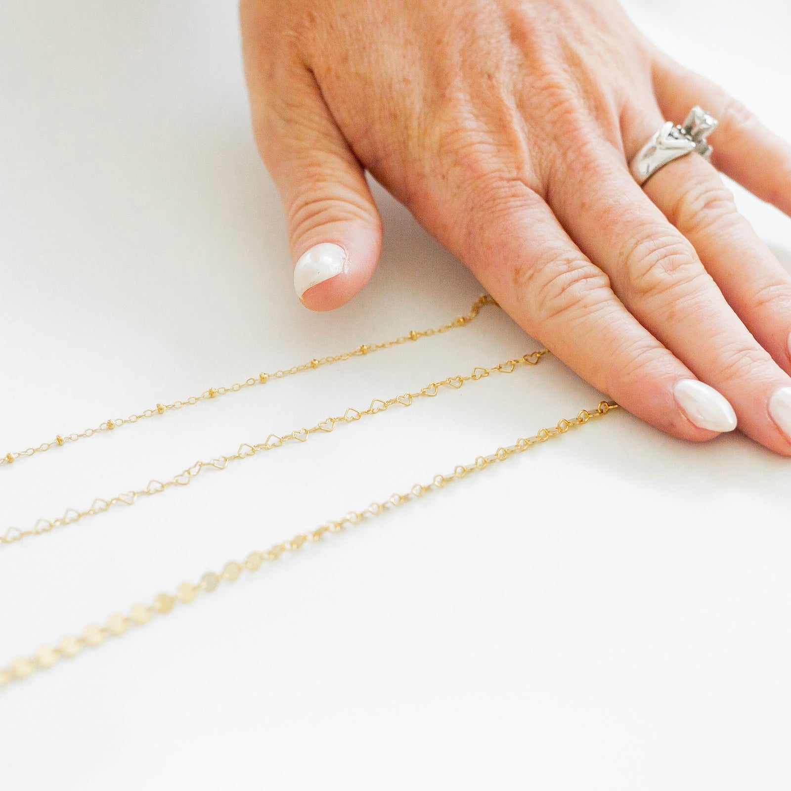 Gold chains displayed on a hand with a ring on a white background
