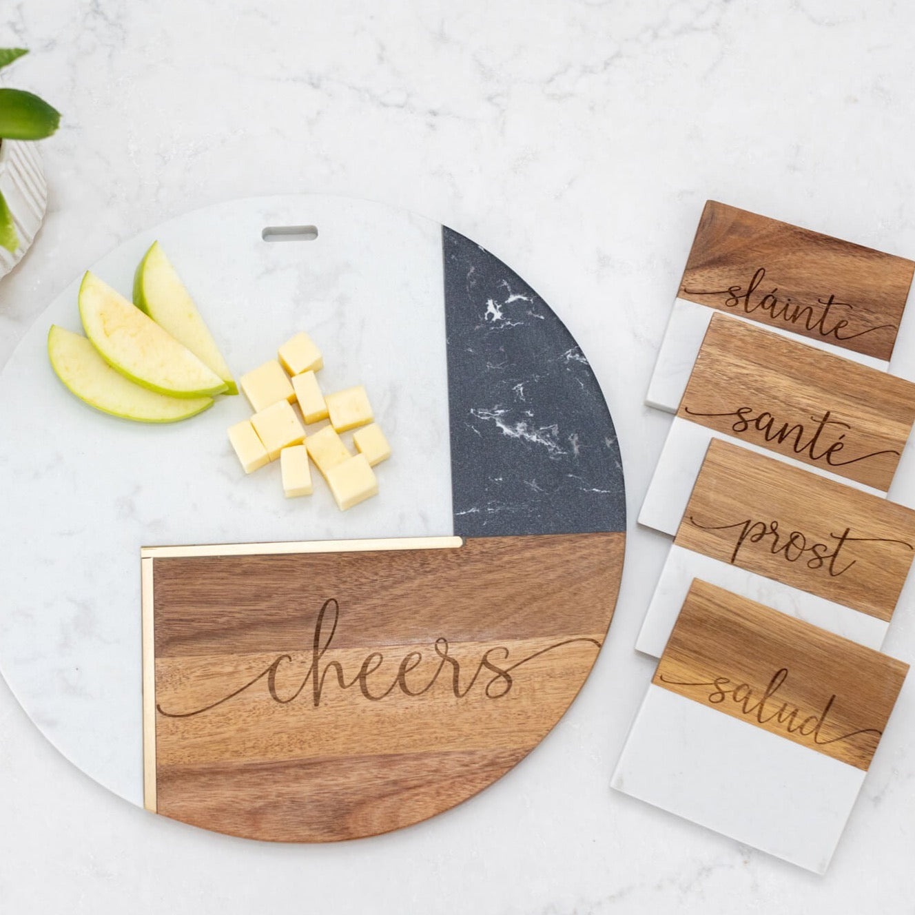 a fit box filled with four stemless wine glasses, four marble and wood coasters, and a round marble and wood charcuterie board. all items are engraved with international terms for "cheers". 