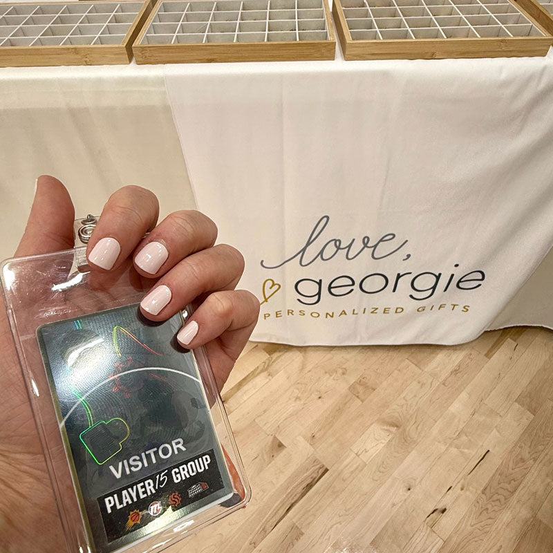 Hand holding a visitor badge with 'Love, Georgie' branded backdrop