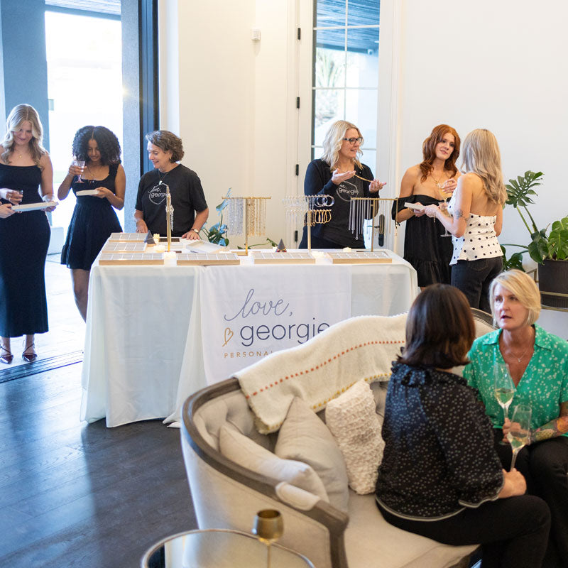 Event with women gathered around a table with 'Love. Georgie' branding, seated on a couch.