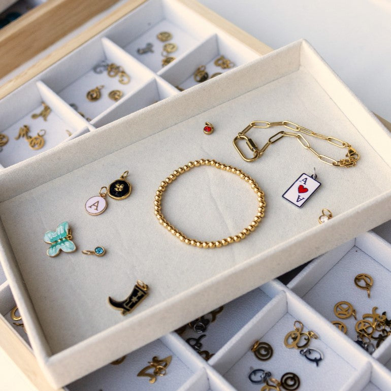 Jewelry set including a gold bracelet, charms, and pendants in a display case.