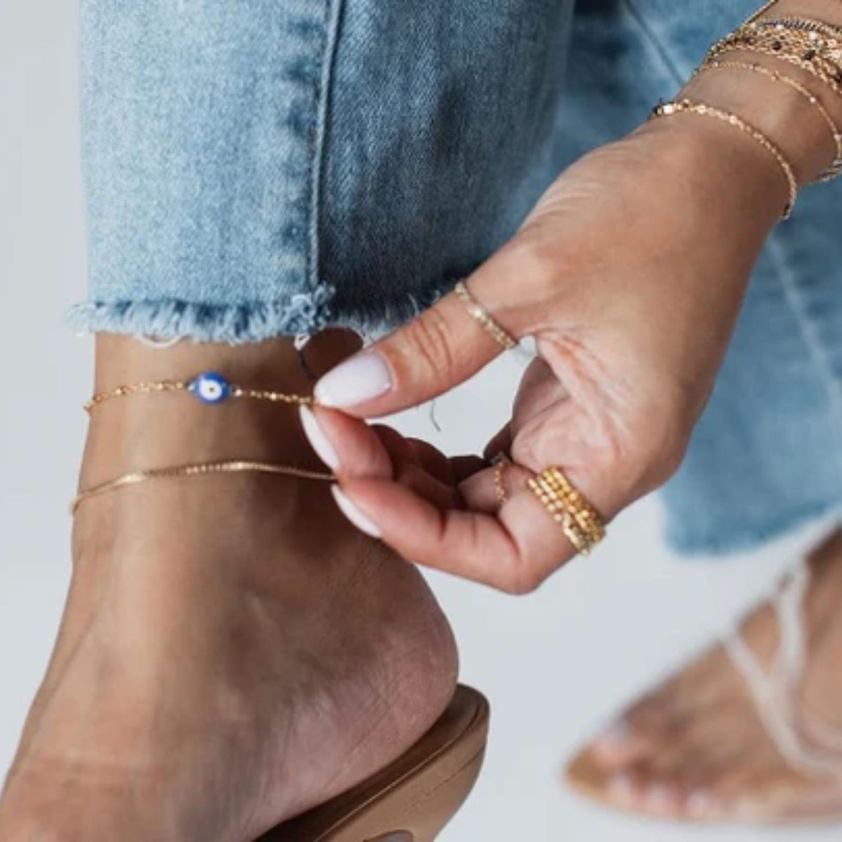 Close-up of a person's foot wearing gold anklets with a plain background