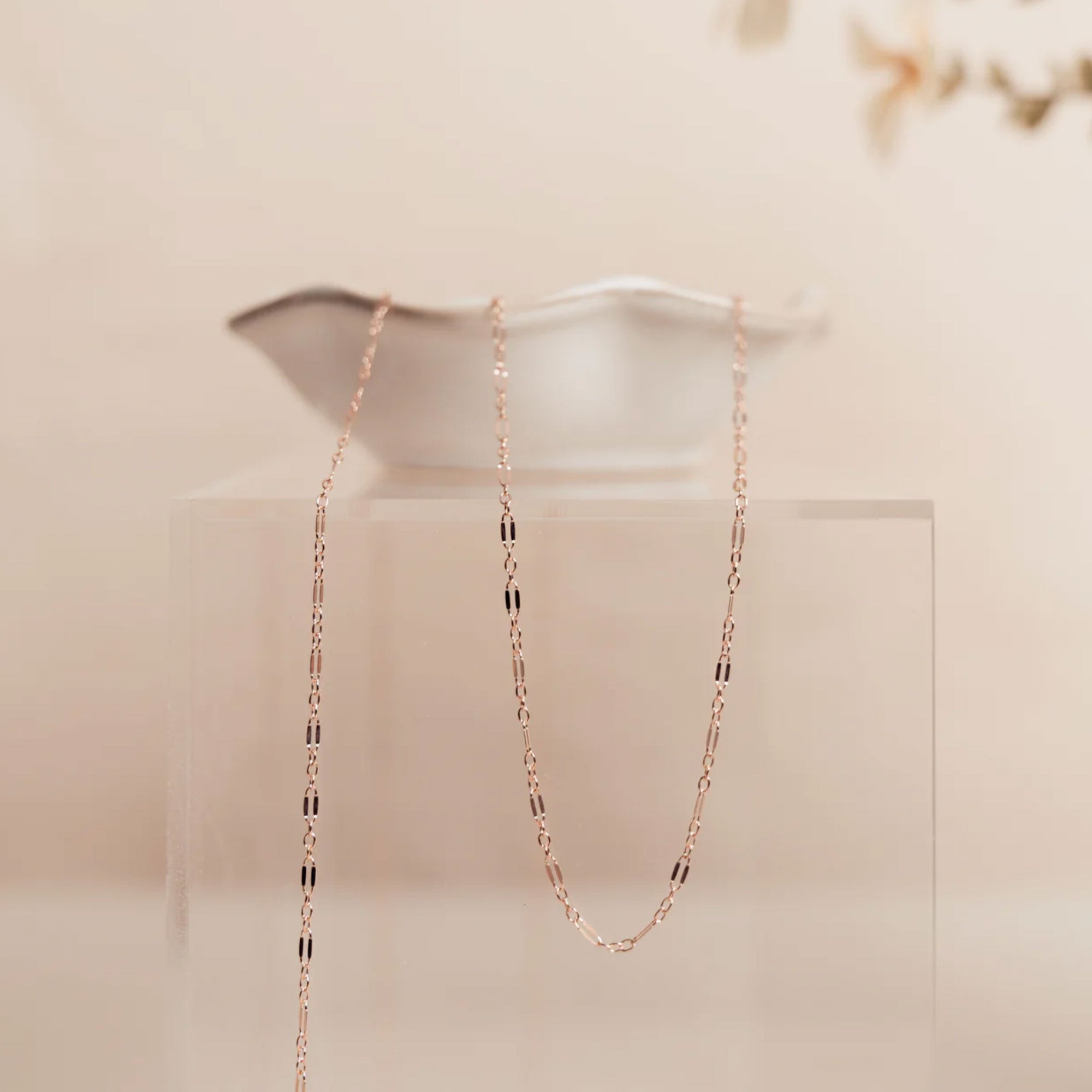Rose gold chain necklace on a white stand with a soft beige background