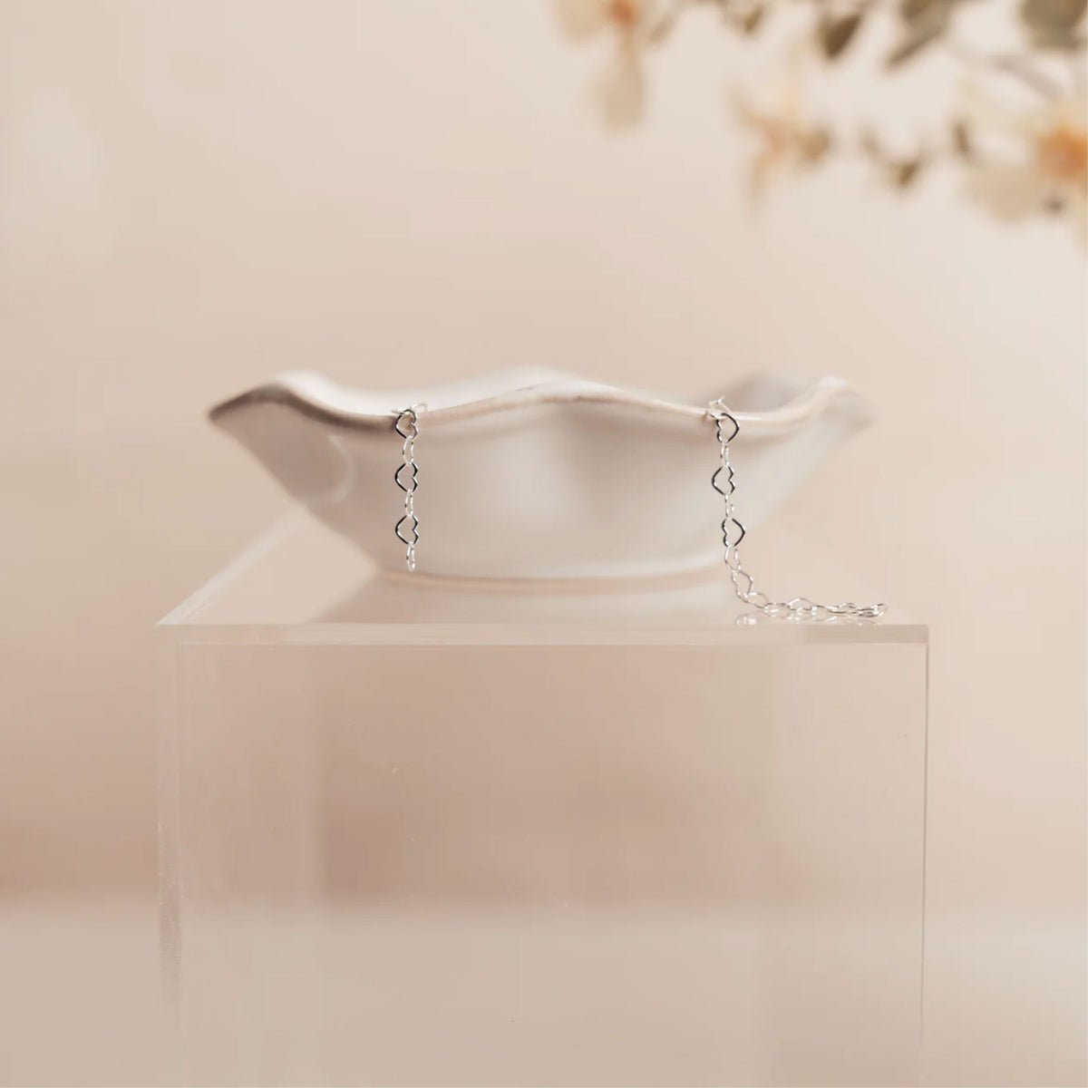 Silver bracelet with heart-shaped charms on a clear stand against a soft beige background
