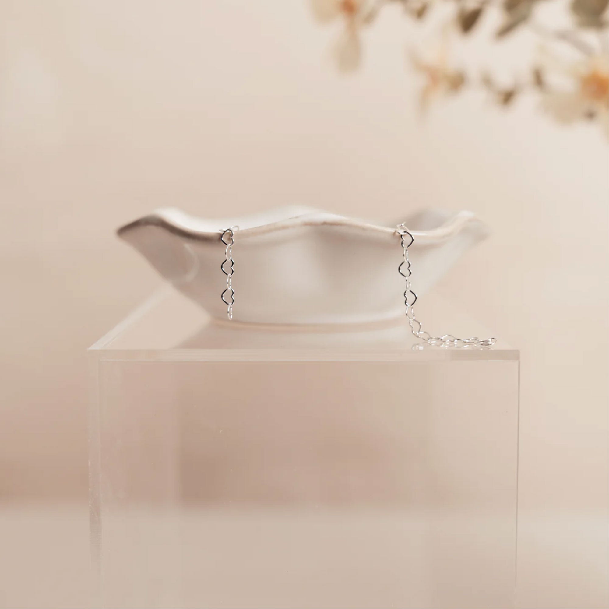 Silver bracelet with heart-shaped charms on a clear stand against a soft beige background