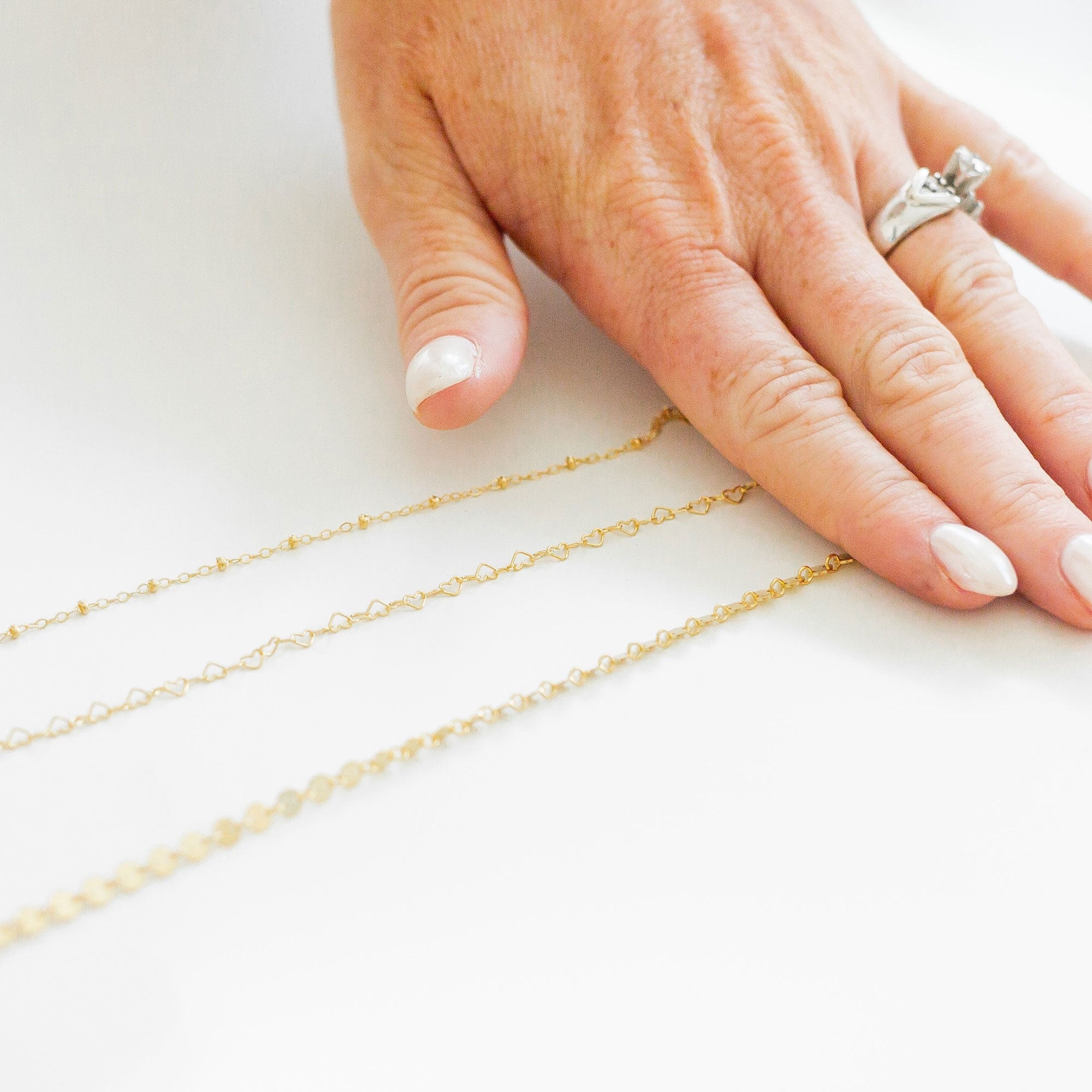 Gold chains displayed on a hand with a ring on a white background