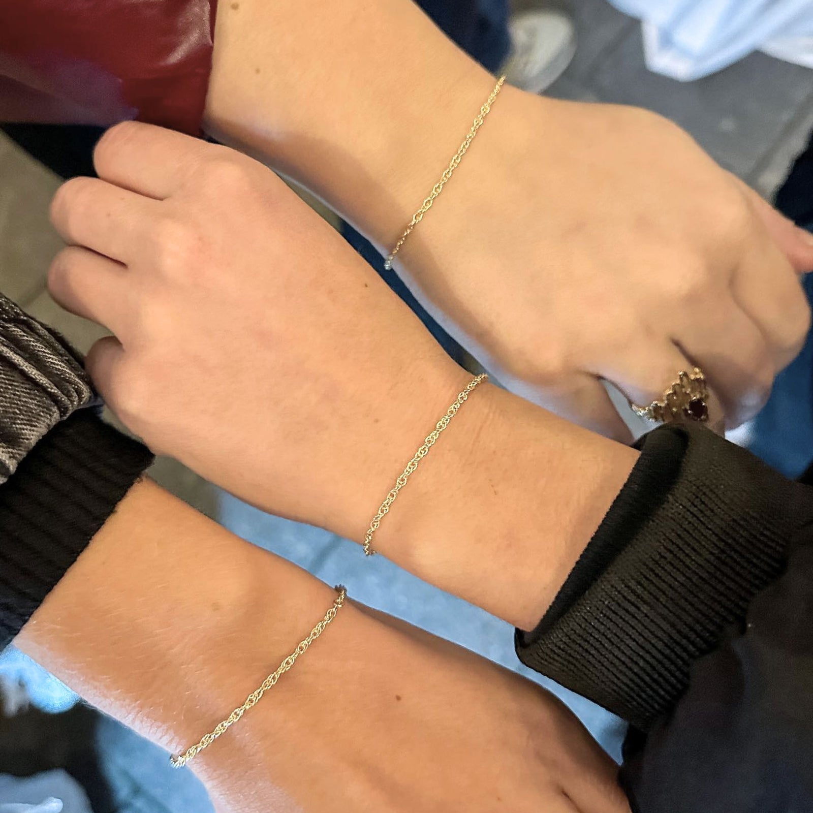 Three wrists wearing gold bracelets with a blurred background
