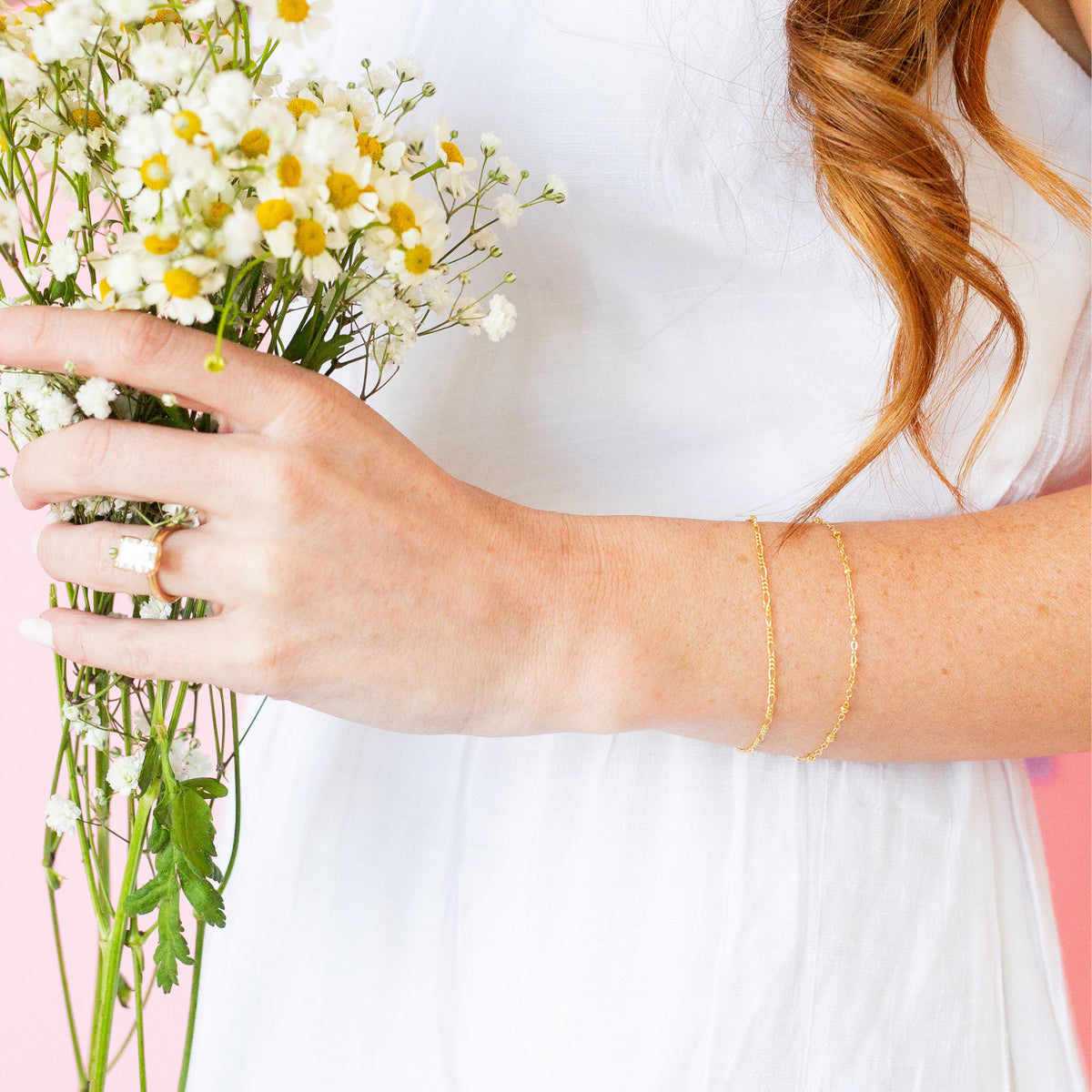 Person holding a bouquet of flowers, wearing two thin gold bracelets