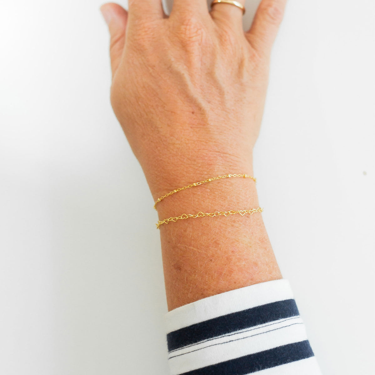 Hand wearing two thin gold bracelets on a white background