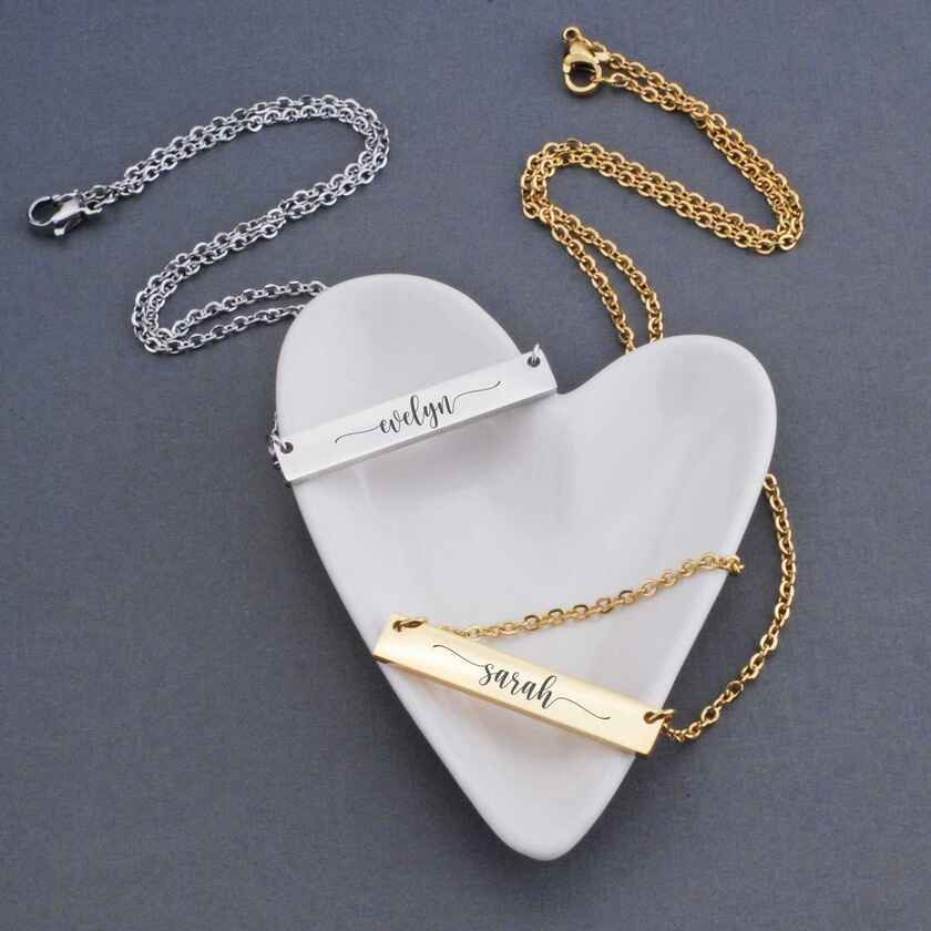 a pair of horizontal bar necklaces, one in silver and another in gold. each is engraved with a woman's first name.