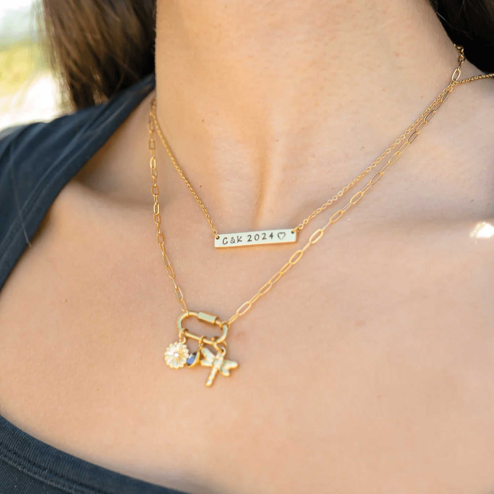Gold necklace with charms and a bar necklace on a person's neck.