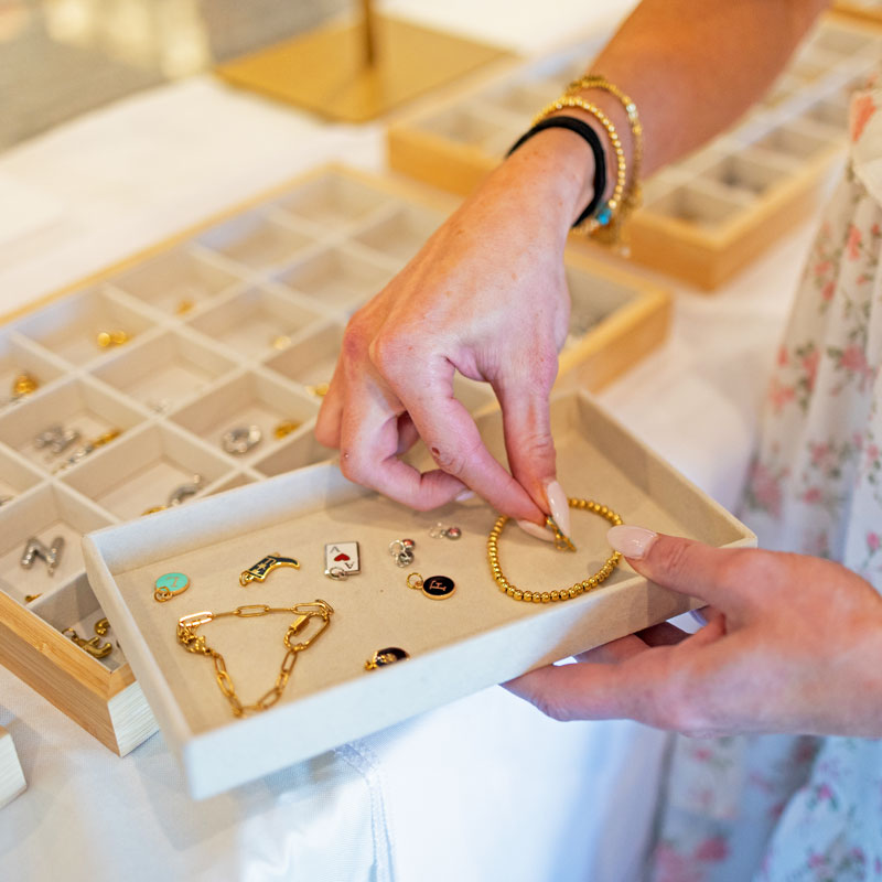 Person selecting jewelry from a display case with a focus on charms and bracelets.