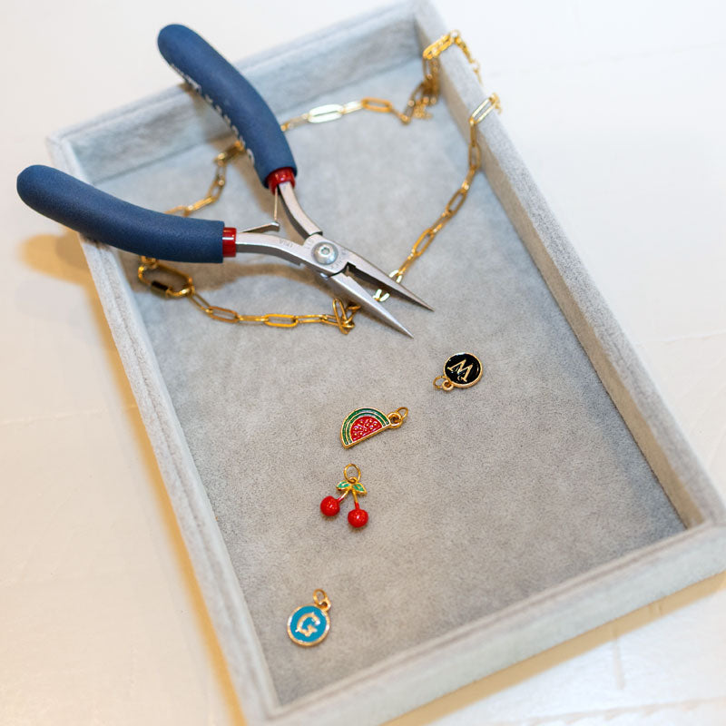 Jewelry-making tools and charms on a gray tray with a white background