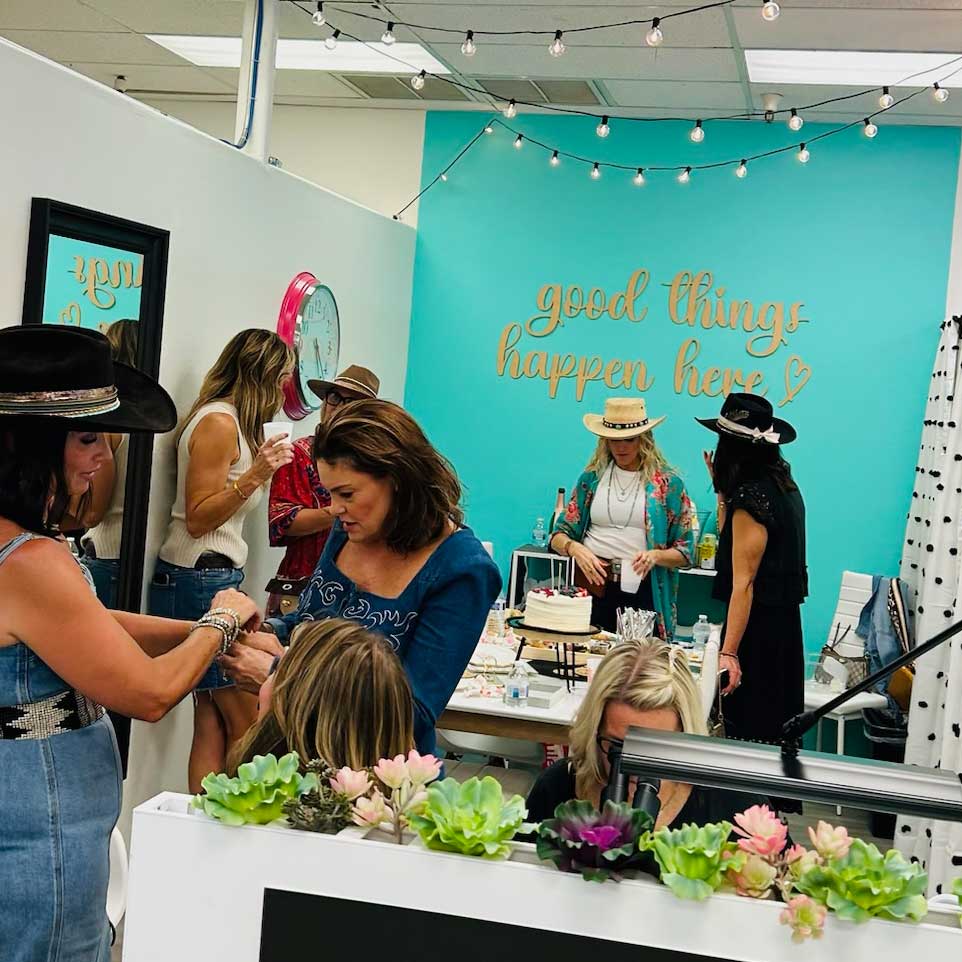 Event or workshop with people around a table with cake and flowers, against a teal wall with 'good things happen here' text.