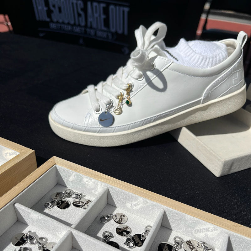 White sneaker with decorative elements on a dark surface, next to a jewelry box with charms.