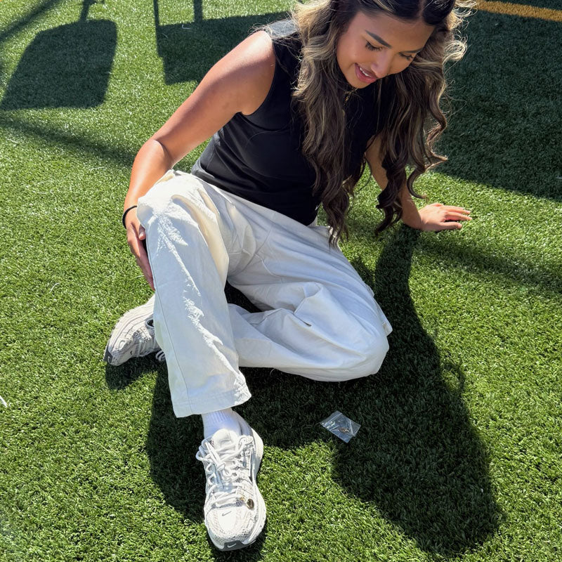 Woman sitting on grass wearing a black top and white pants looking at a charm accessory.