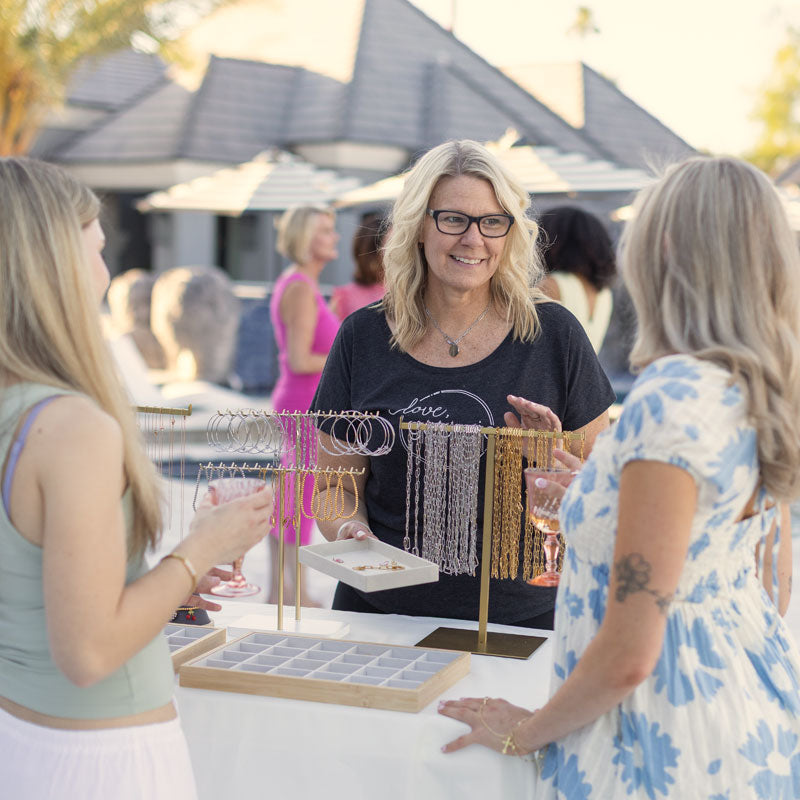 Woman at a jewelry booth interacting with two other women outdoors.