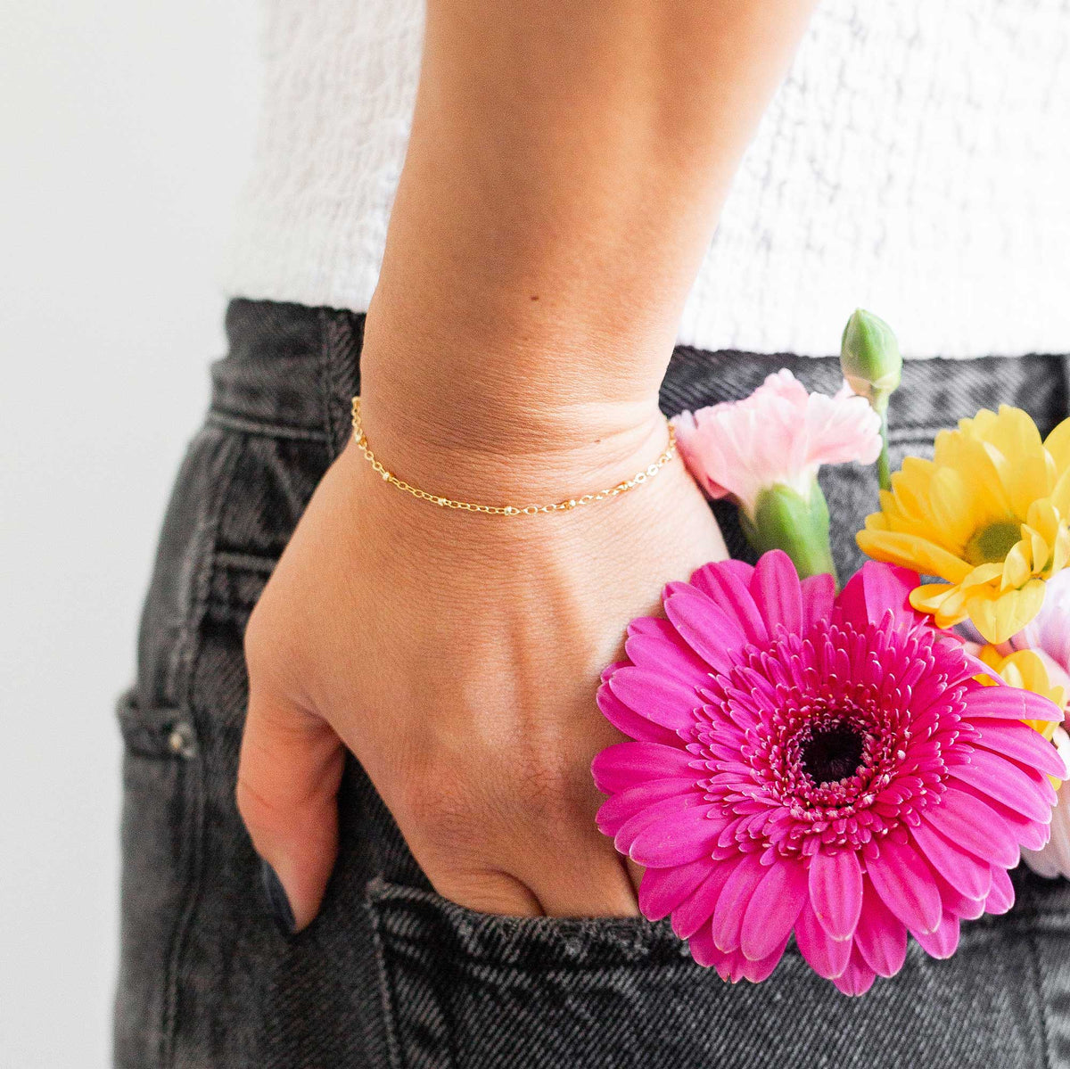 Hand with a thin gold bracelet on tucked into her back jeans pocket with a bouquet of flowers in it with a blurred background