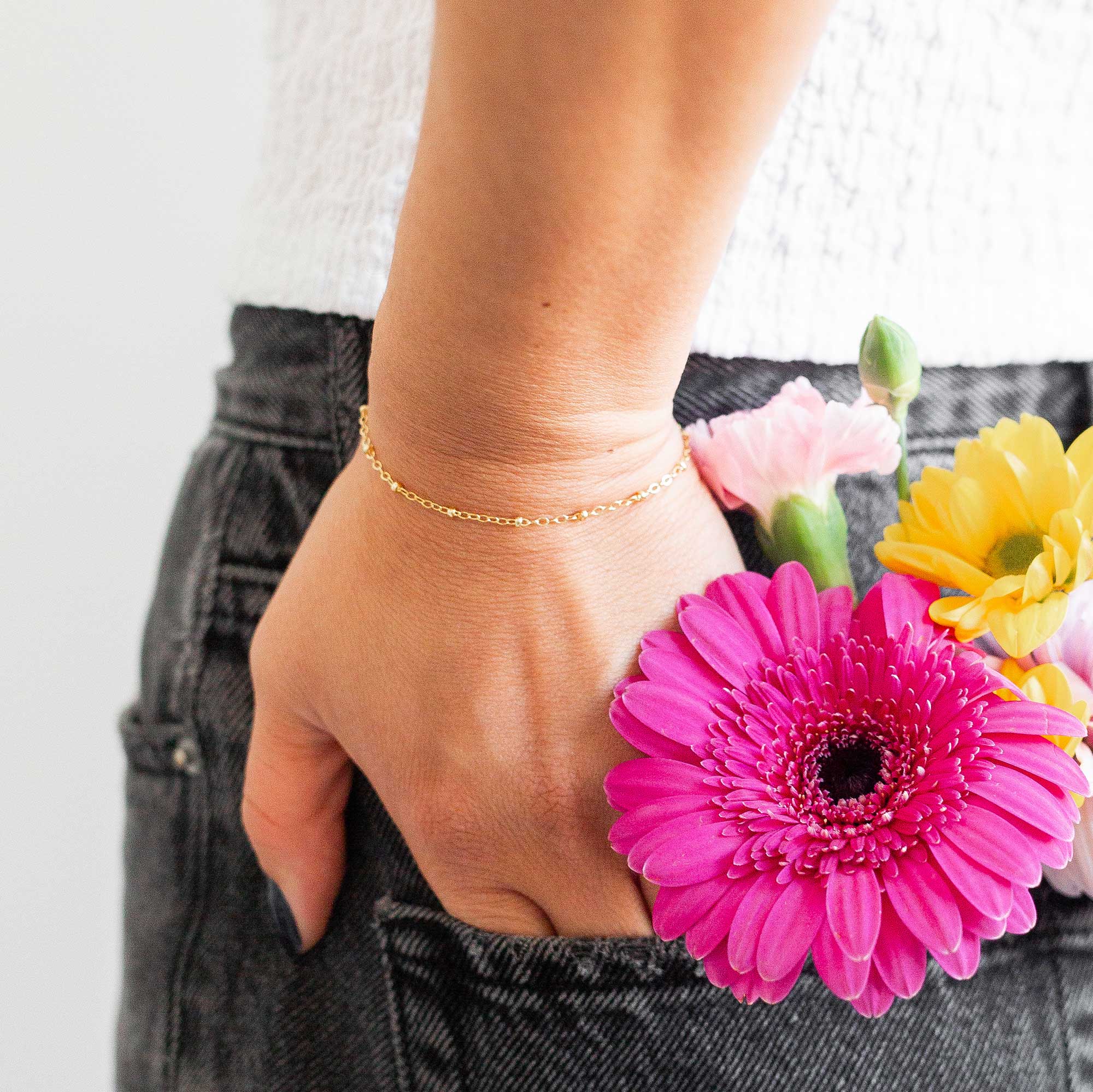 Hand with a thin gold bracelet on tucked into her back jeans pocket with a bouquet of flowers in it with a blurred background