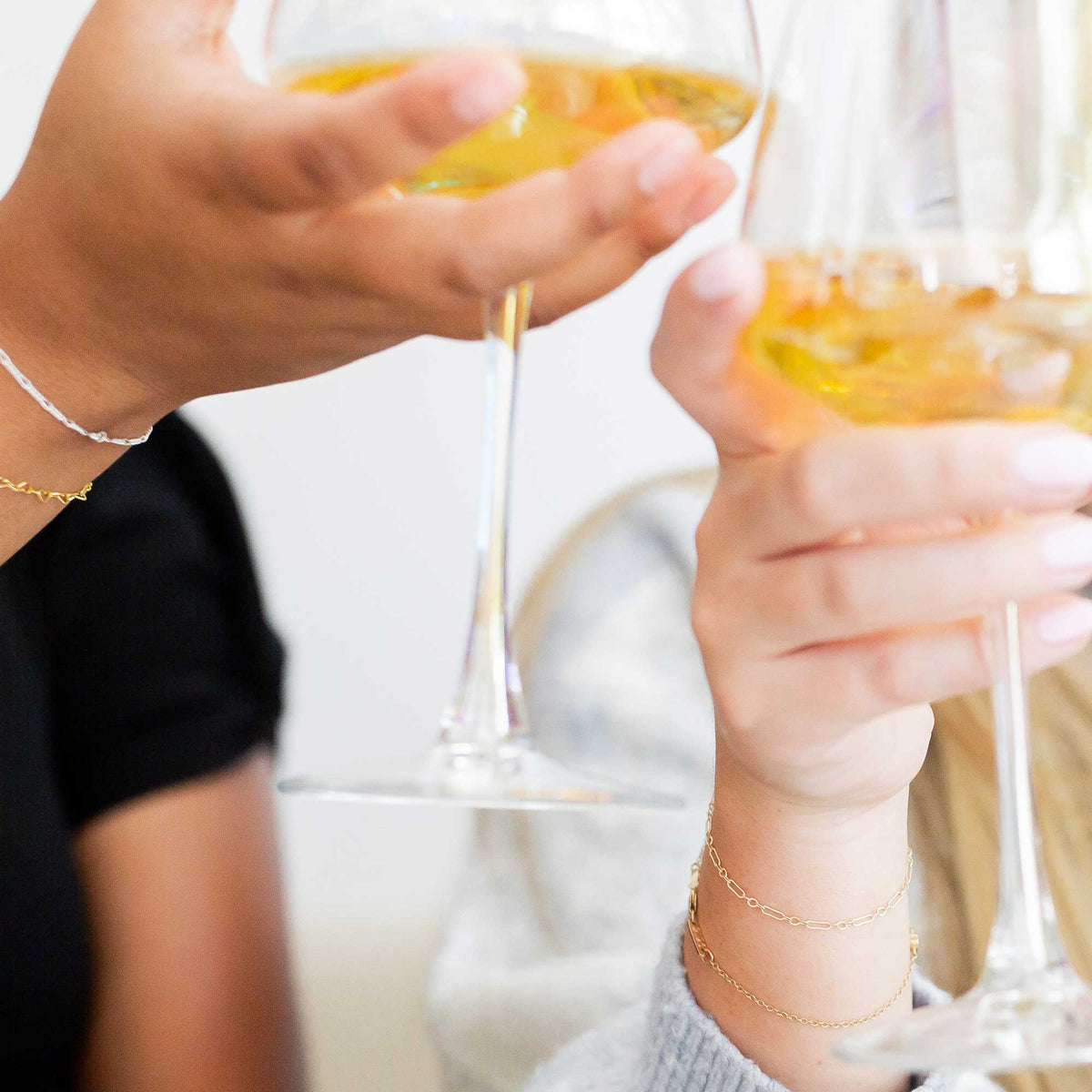 Two people clinking champagne glasses with a blurred background displaying their Love, Georgie bracelets.