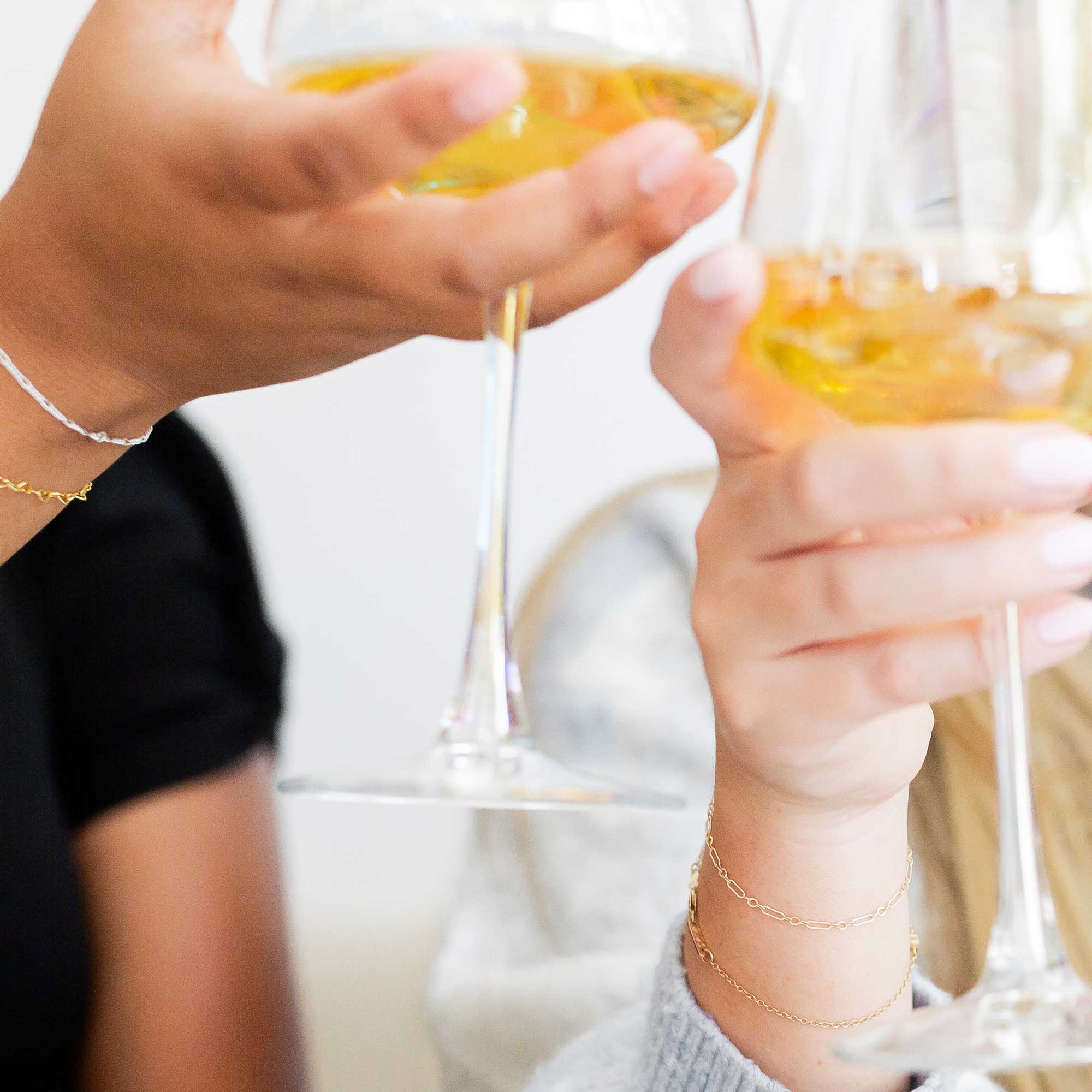 Two people clinking champagne glasses with a blurred background displaying their Love, Georgie bracelets.