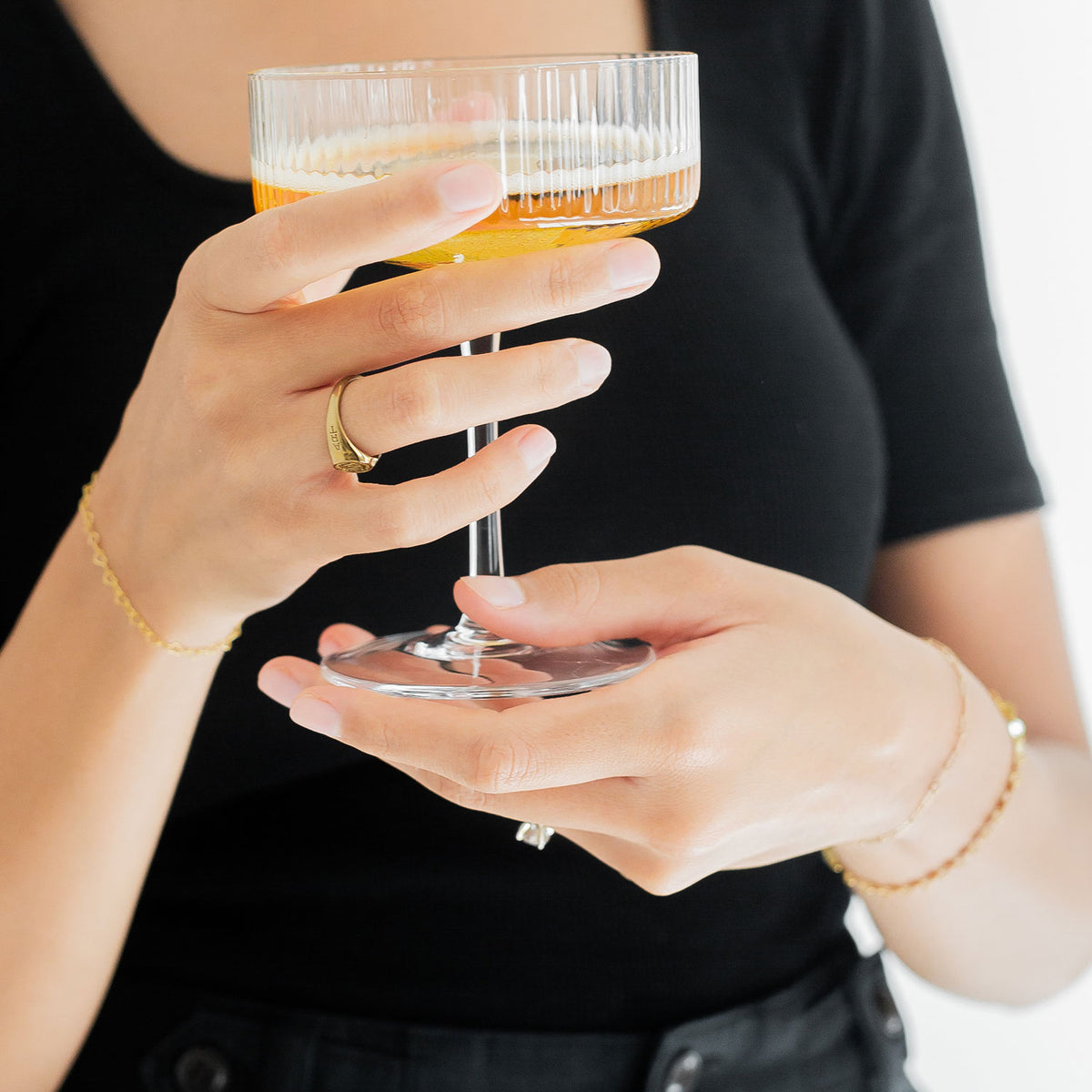 Two hands holding a glass with bracelets displayed on both wrists